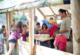 Kinderen en volwassenen maken ballonfiguren onder een houten afdak bij Huttopia Lac de Sillé glamping.