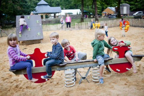 Kinder spielen auf einer Wippe im Sandspielplatz bei Huttopia Lac de Sillé - Glamping Pays de la Loire.