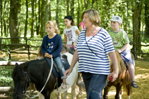 Children ride ponies led by an adult in a forest at Huttopia Lac de Sillé glamping, Pays de la Loire, France.