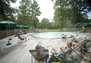 Familias descansan en tumbonas junto a la piscina rodeada de árboles en Huttopia Lac de Sillé Glamping.