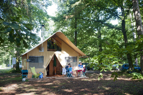 Glampingophold ved Huttopia Lac de Sillé i Pays de la Loire, familie uden for telt omgivet af skov.