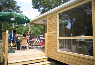 Famiglia che si gode un pasto sulla veranda di una cabina a Huttopia Lac de Sillé, Glamping Pays de la Loire.