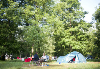 Famiglia in campeggio vicino a una tenda tra alberi verdi a Huttopia Lac de Sillé, glamping Pays de la Loire.
