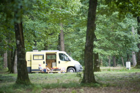 Man relaxing outside a yellow camper van in the woods at Huttopia Lac de Sillé glamping, Pays de la Loire.