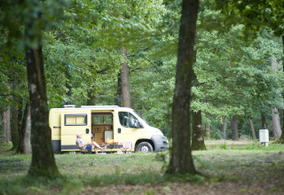 Homme assis devant un van jaune dans les bois à Huttopia Lac de Sillé glamping, Pays de la Loire.