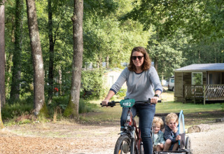 Vrouw fietst met twee kinderen in aanhanger bij Huttopia Lac de Sillé - Glamping Pays de la Loire.