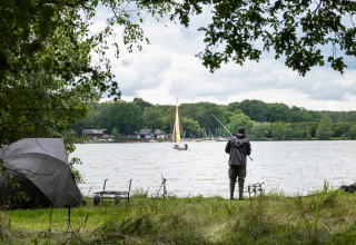 Persona che pesca vicino a una tenda al glamping Huttopia Lac de Sillé, Pays de la Loire, immerso nella natura.
