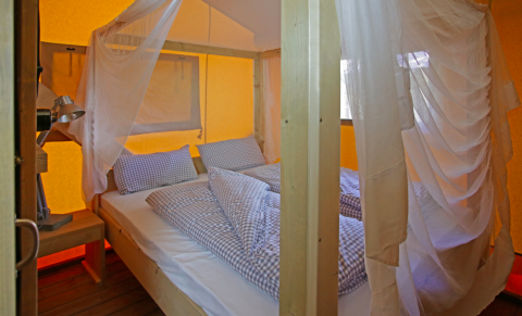 Vista interior de una Nature Lodge en Azur Camping Altmühle, Kipfenberg, con cama cómoda y mosquitera.