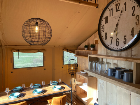 Interior view of cozy glamping accommodation at Azur Camping Altmühle with dining table and large wall clock.