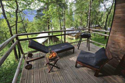 Træterrasse med liggestole, bord med frugt og grill på Nature Resort Natterer See Safarilodges Tirol i skoven.
