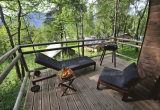 Houten terras met ligstoelen, fruitschaal en barbecue bij Nature Resort Natterer See Safarilodges Tirol in het bos.
