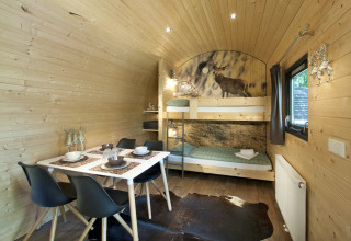 Vista interior de alojamiento glamping con literas, mesa de comedor y decoración de madera en Nature Resort Natterer See.