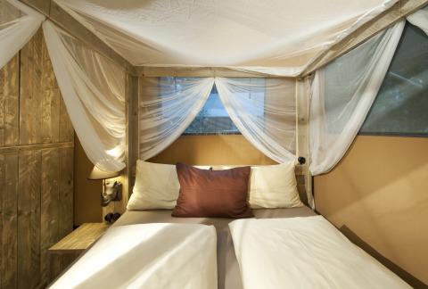 Chambre chaleureuse avec lit double et moustiquaire dans une tente glamping du Nature Resort Natterer See, Tirol.