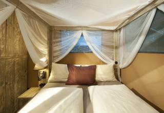 Cozy bedroom with double bed and mosquito net in glamping tent at Nature Resort Natterer See, Tirol.