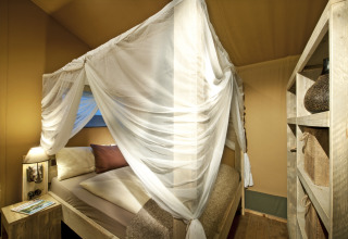 Intérieur d’une safarilodge de luxe au Nature Resort Natterer See avec lit à baldaquin et mobilier en bois.