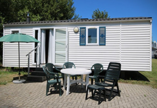 Alojamiento glamping moderno en Camping Naumburg, Hessen, con terraza, sillas de plástico y sombrilla verde.