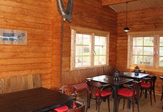 Interior de una cabaña de madera en Camping Naumburg - Glamping Hessen con mesas, sillas y ventanas grandes.