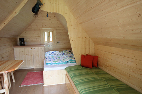 Hyggelig indretning i glampinghytte med trævægge, seng, sofa og lille køkken i Camping Naumburg, Hessen.