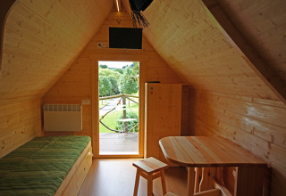 Vue intérieure d'une cabane de glamping confortable avec murs en bois, lit, table et vue sur la verdure.