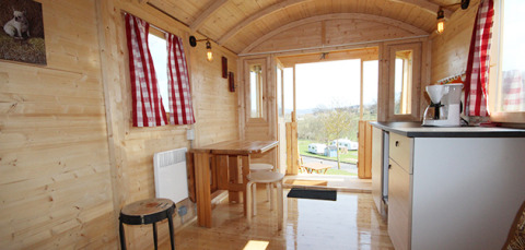 Interior of cozy glamping accommodation at Camping Naumburg - Glamping Hessen with wood paneling and checkered curtains.