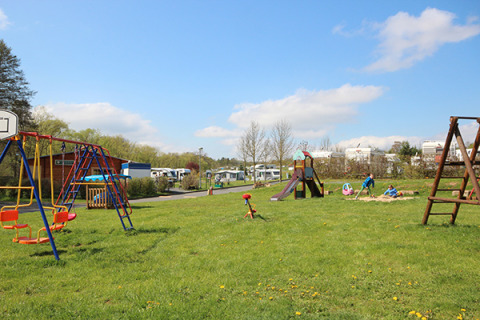 Speeltuin bij Camping Naumburg - Glamping Hessen met schommels, glijbaan en spelende kinderen in de zon.