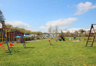 Spielplatz auf dem Camping Naumburg - Glamping Hessen mit Schaukeln, Rutsche und Kindern beim Spielen.