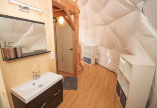 Interior de glamping en Domaine la Chabanne - Domes Auvergne-Rhône-Alpes, con lavabo, madera y estanterías blancas.