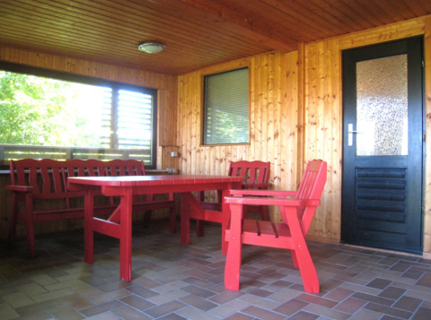 Overdekt terras van Campingpark Lindelgrund - Chalets Rheinland-Pfalz met rode houten meubels en houten wanden.