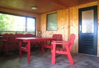 Indendørs terrasse i Campingpark Lindelgrund - Chalets Rheinland-Pfalz med røde træmøbler og trævægge.
