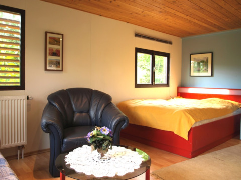 Interior de un acogedor chalet en Campingpark Lindelgrund con cama doble, sillón y mesa de centro.
