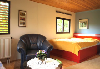 Innenansicht eines gemütlichen Chalets im Campingpark Lindelgrund mit Bett, Sessel und Couchtisch.