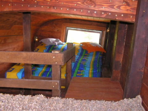 Cozy sleeping area inside a glamping train car featuring colorful bedding and rustic wood walls.