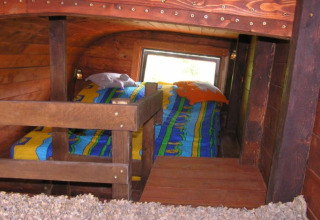 Accogliente area notte in una carrozza ferroviaria glamping con biancheria colorata e pareti in legno.