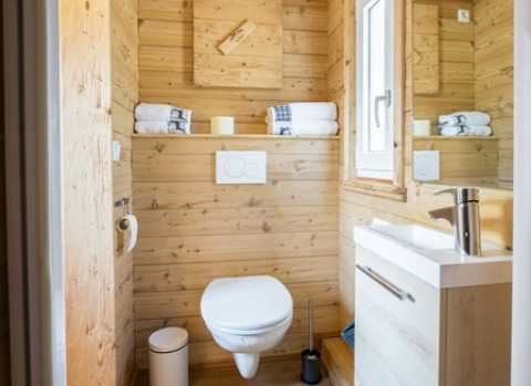 Modernes Badezimmer aus Holz im Seecamping Appesbach Tiny House, mit Fenster, weißen Handtüchern und Spiegel.