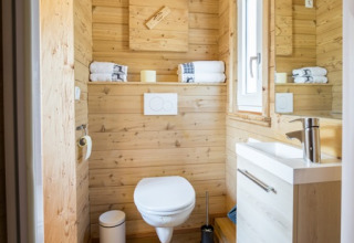 Modernes Badezimmer aus Holz im Seecamping Appesbach Tiny House, mit Fenster, weißen Handtüchern und Spiegel.