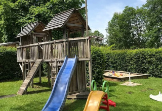 Playground at Camping Wallersee - Stacaravans Salzburg with slides, wooden playhouse and sandbox on grass.