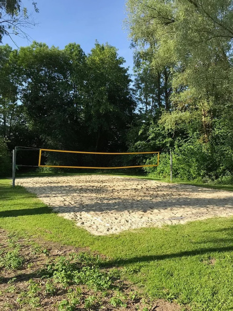 Cancha de voleibol de arena en Camping Wallersee - Stacaravans Salzburg, rodeada de árboles verdes.