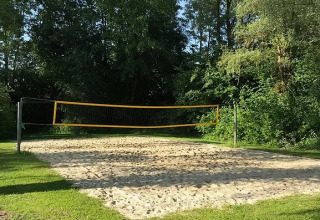Zandvolleybalveld op Camping Wallersee - Stacaravans Salzburg, omgeven door groen en bomen.