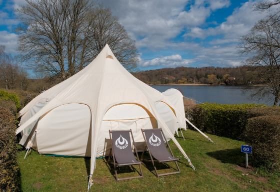 Grande tente de glamping avec deux transats devant au bord d'un lac au Natuurpark Camping Prinzenholz, Schleswig-Holstein.
