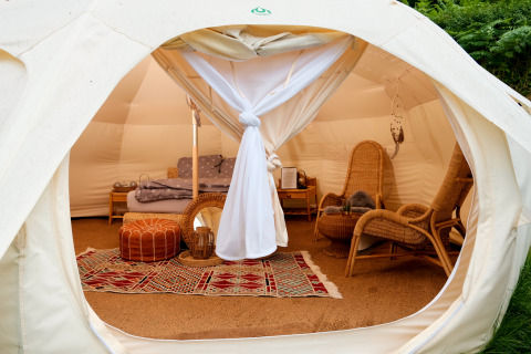 Innenansicht einer Glamping-Unterkunft mit gemütlichen Sesseln, Bett und farbigem Teppich im Zelt.