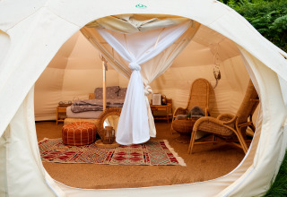 Innenansicht einer Glamping-Unterkunft mit gemütlichen Sesseln, Bett und farbigem Teppich im Zelt.