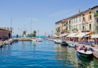 Vista sul lago di Garda con barche, edifici colorati e passeggiata vicino a Vacanze Glamping Boutique.