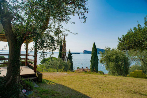 Terraza de alojamiento glamping con vistas al Lago de Garda, rodeada de árboles verdes y aguas azules claras.
