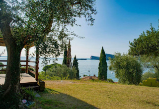 Terrazza dell’alloggio glamping con vista sul Lago di Garda, circondata da alberi verdi e acqua limpida.