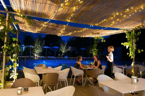 Gemütlicher Außenbereich eines Glamping-Platzes bei Nacht, Lichterketten und Blick auf einen beleuchteten Pool.