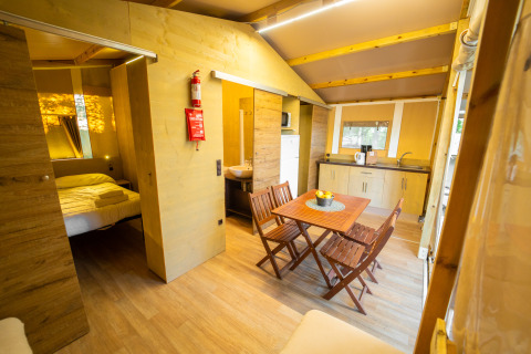Innenansicht eines luxuriösen Glamping-Zeltes mit Holzmöbeln, Schlafzimmer, Küche und Essbereich.