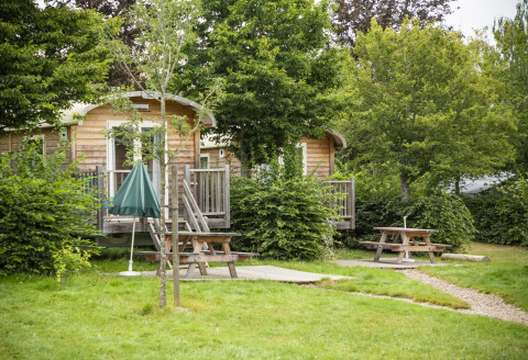 Houten hutten en picknickbanken in het groen bij Huttopia Etang de Fouché Glamping Bourgogne, Frankrijk.