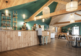Bar y zona de salón del interior en Huttopia Etang de Fouché - Glamping Bourgogne, con paneles de madera y luz cálida.