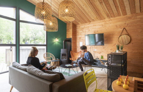 Acogedora sala en Huttopia Etang de Fouché - Glamping Bourgogne, con dos personas, paredes de madera y decoración moderna.