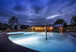 Illuminated swimming pool at dusk at Huttopia Etang de Fouché - Glamping Bourgogne, surrounded by trees.